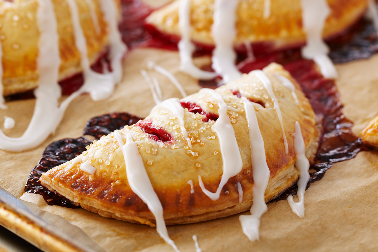 raspberry hand pies on parchment paper drizzled with frosting