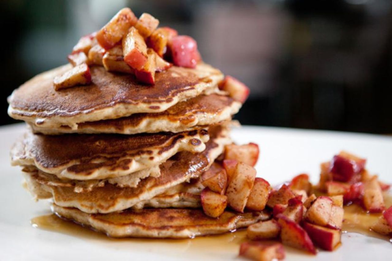 A large stack of Bobby Flay's walnut pancakes topped with syrup and cinnamon apples