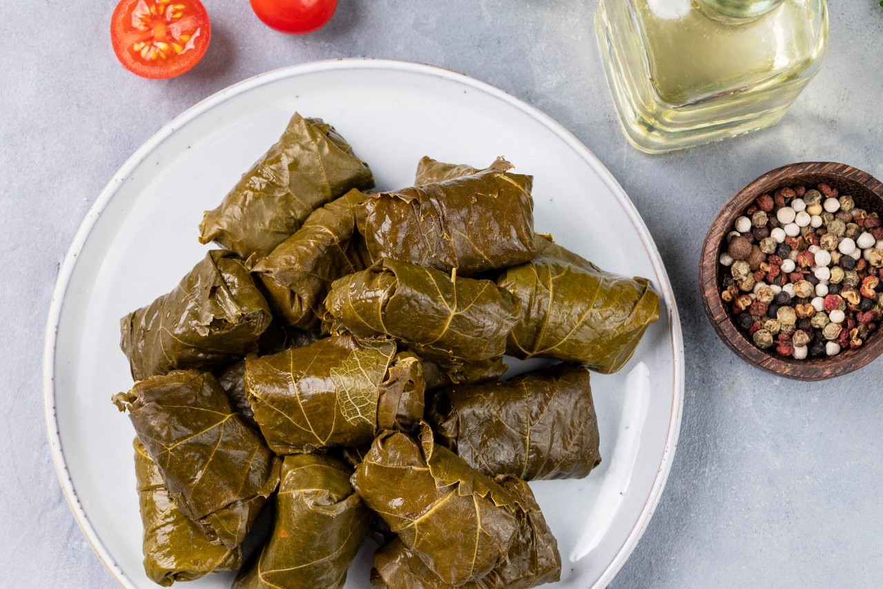 Dolma. Stuffed grape leaves (traditional Caucasian, Turkish, Greek cuisine) on a blue plate with fresh herbs on a light background with olive oil, tomato and pepper. - stock photo