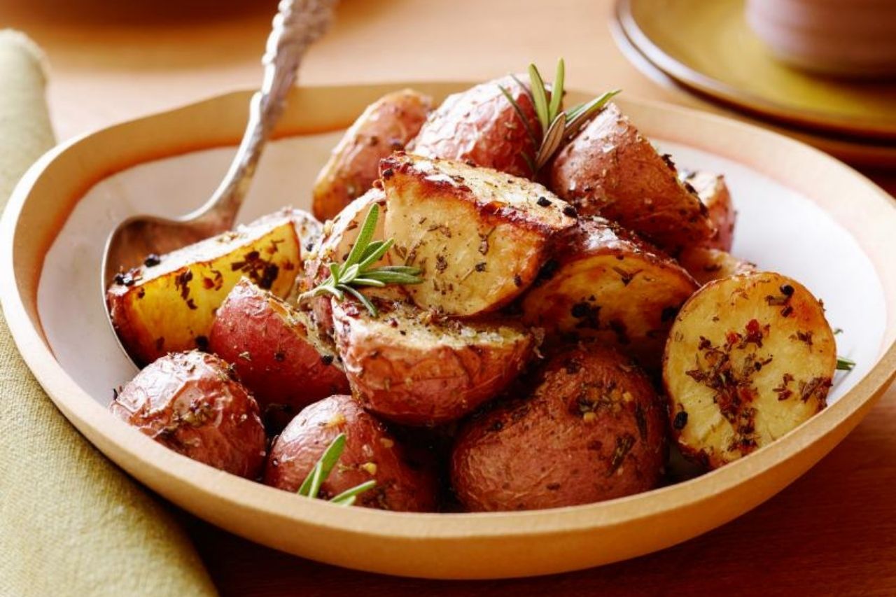 A bowl with oven-baked potatoes cut into quarters and seasoned with spices and fresh rosemary