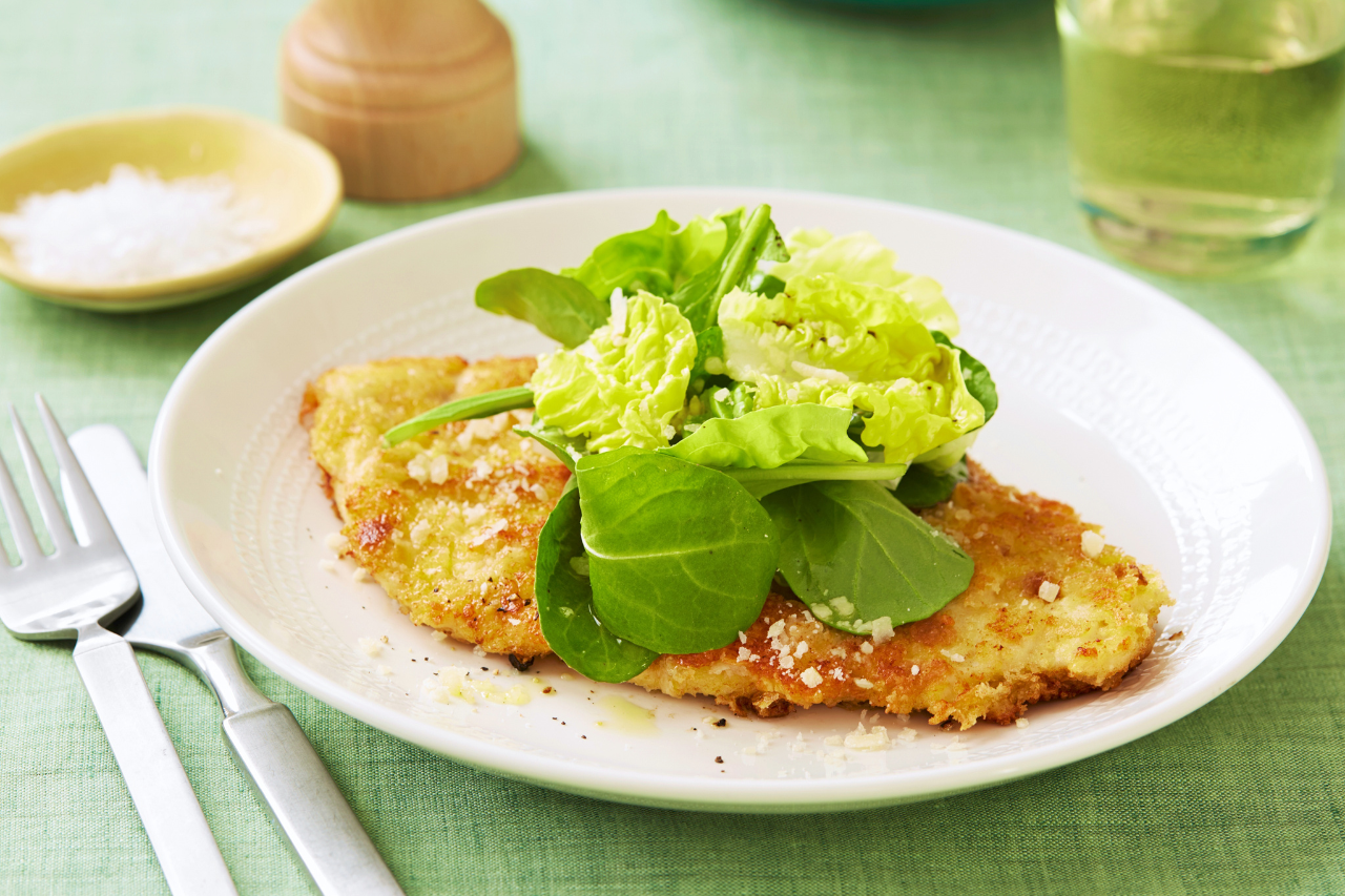 A plate with parmesan chicken topped with fresh greens