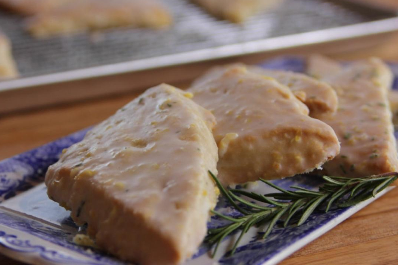 Ree Drummond;s glazed lemon rosemary scones with a fresh sprig of rosemary nearby