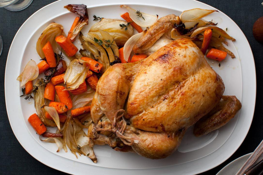 An overhead shot of a whole roast chicken with carrots and onion