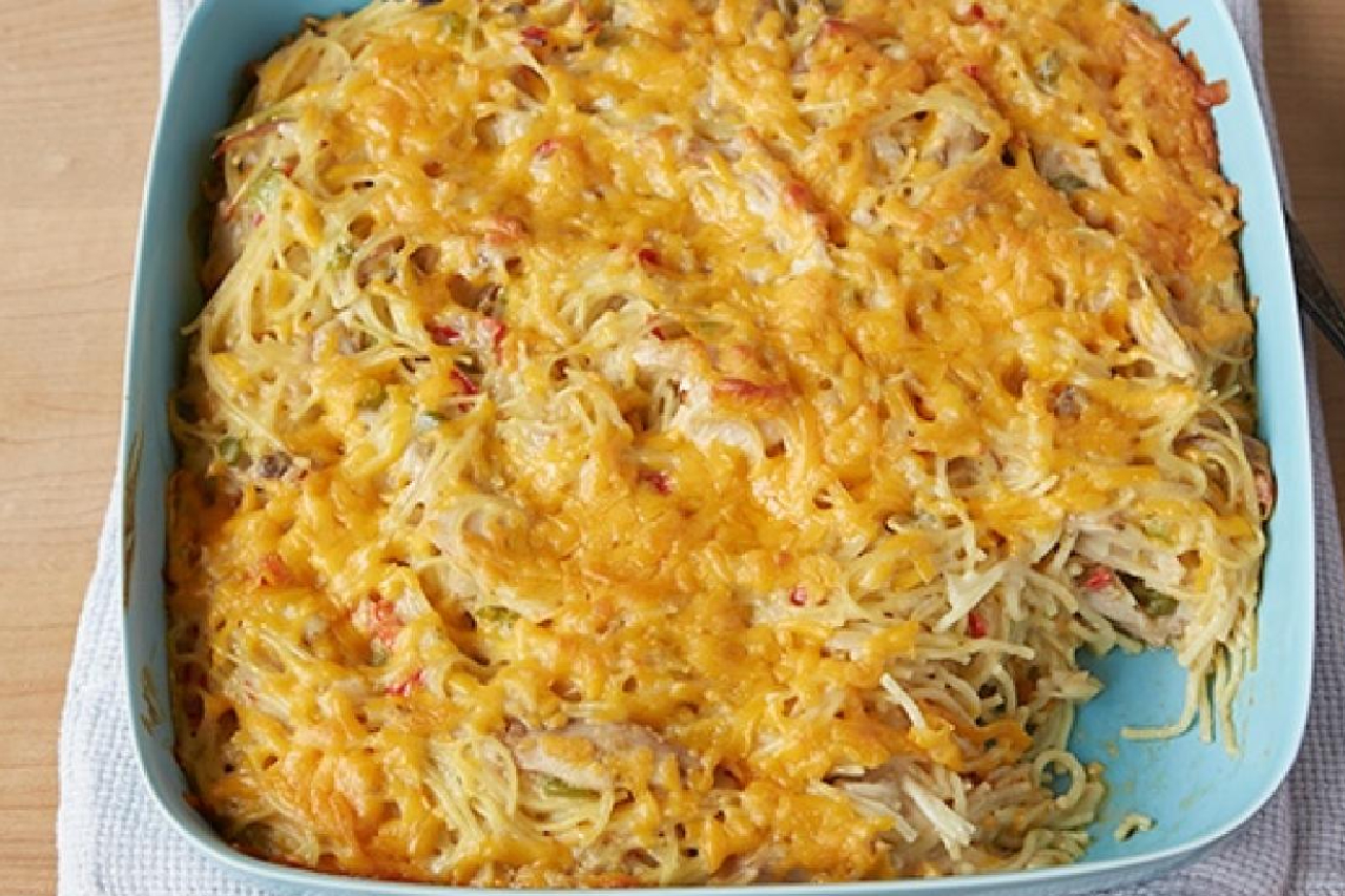 A casserole dish with spaghetti and chicken, covered in a layer of melted cheese