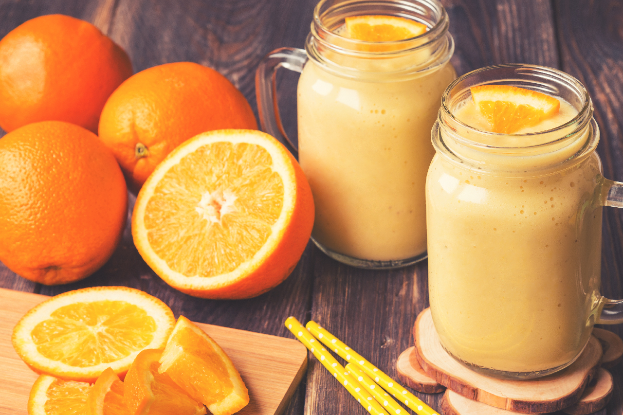 Orange fruit smoothie in the glass jars with fresh orange slices on rustic wooden background. Vintage toned picture.