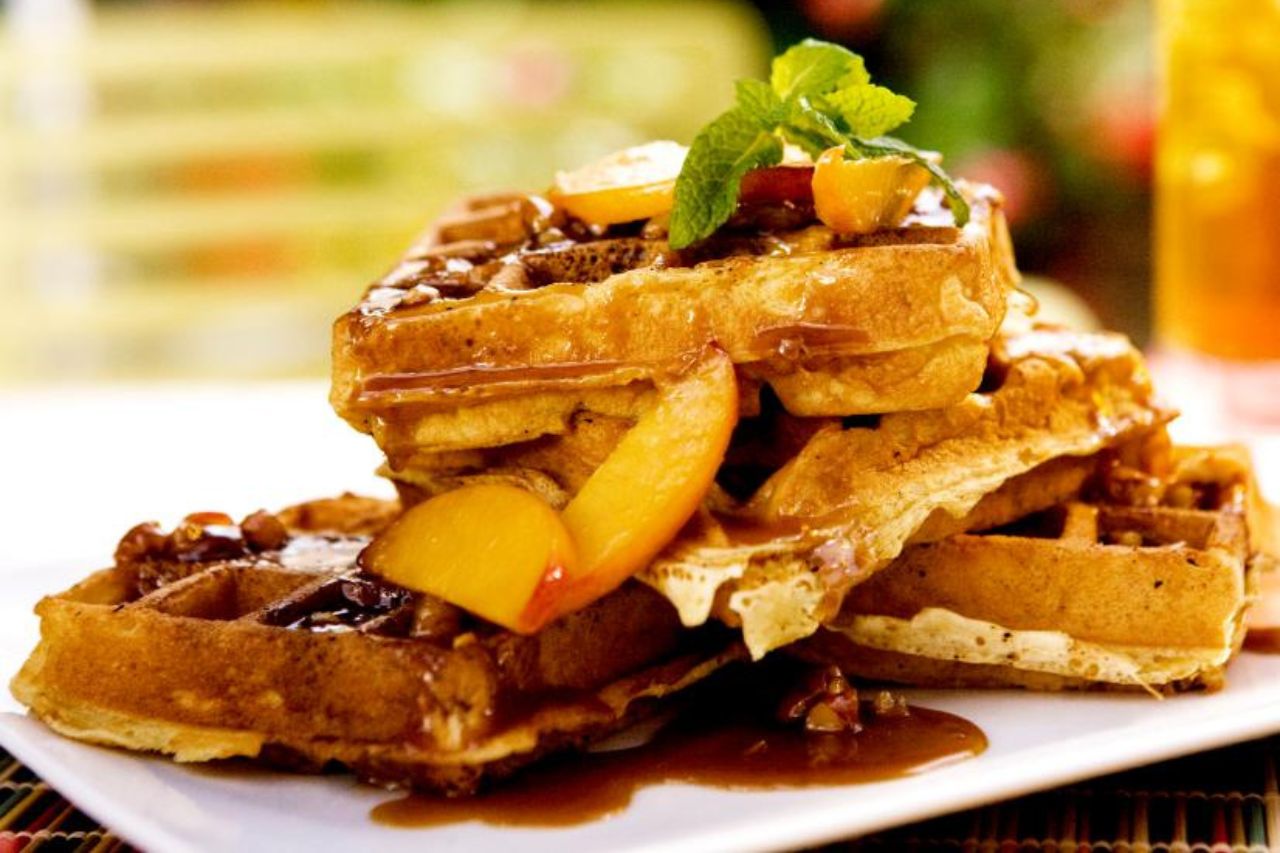 A large stack of waffles with maple syrup and peaches