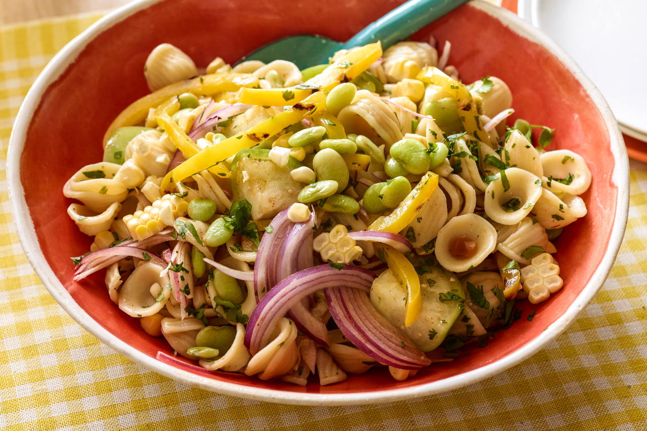 A pasta salad with re onions, edamame, ad grilled corn
