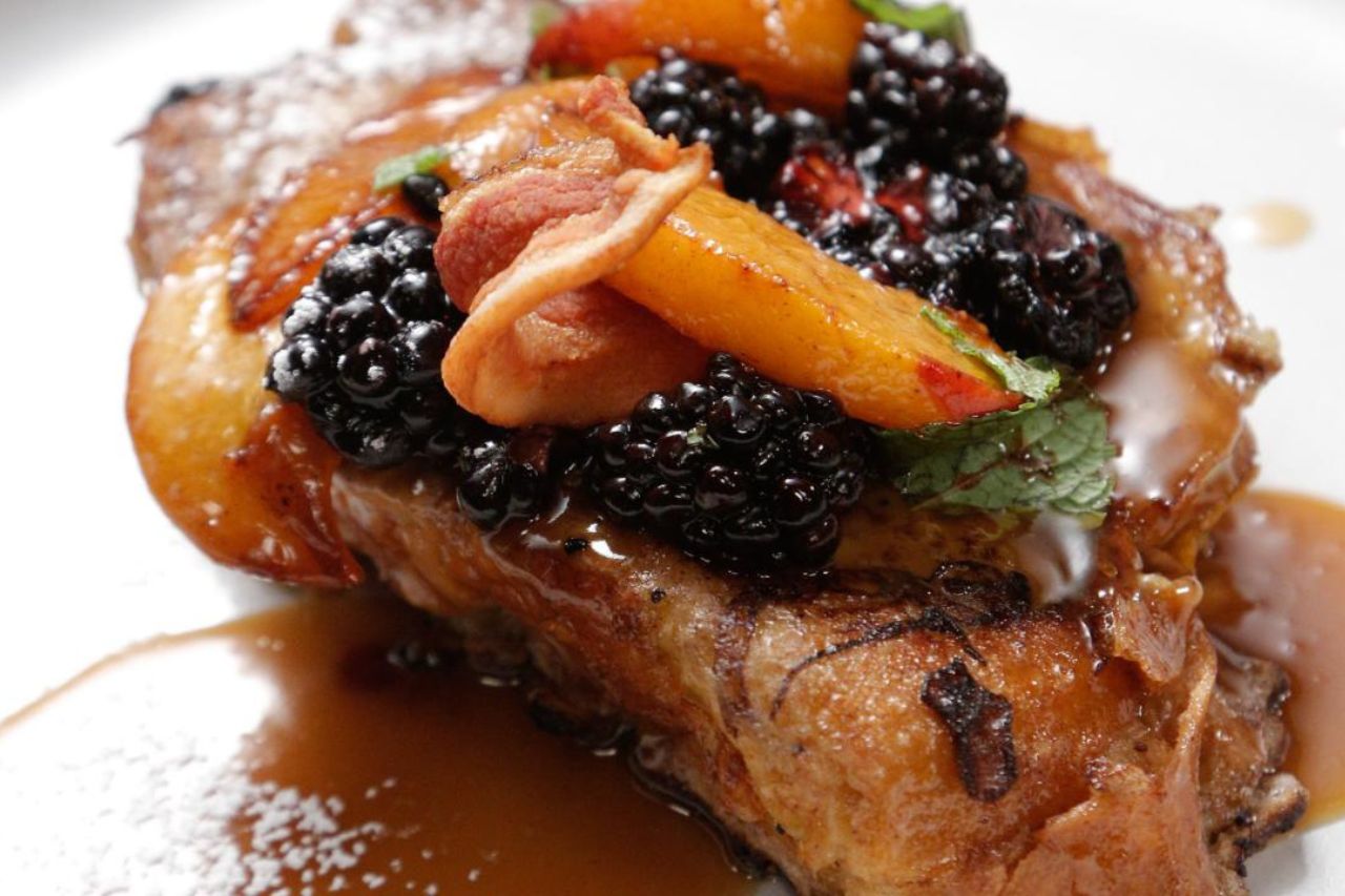 A French toast topped with a bourbon caramel sauce and blackberries and peaches