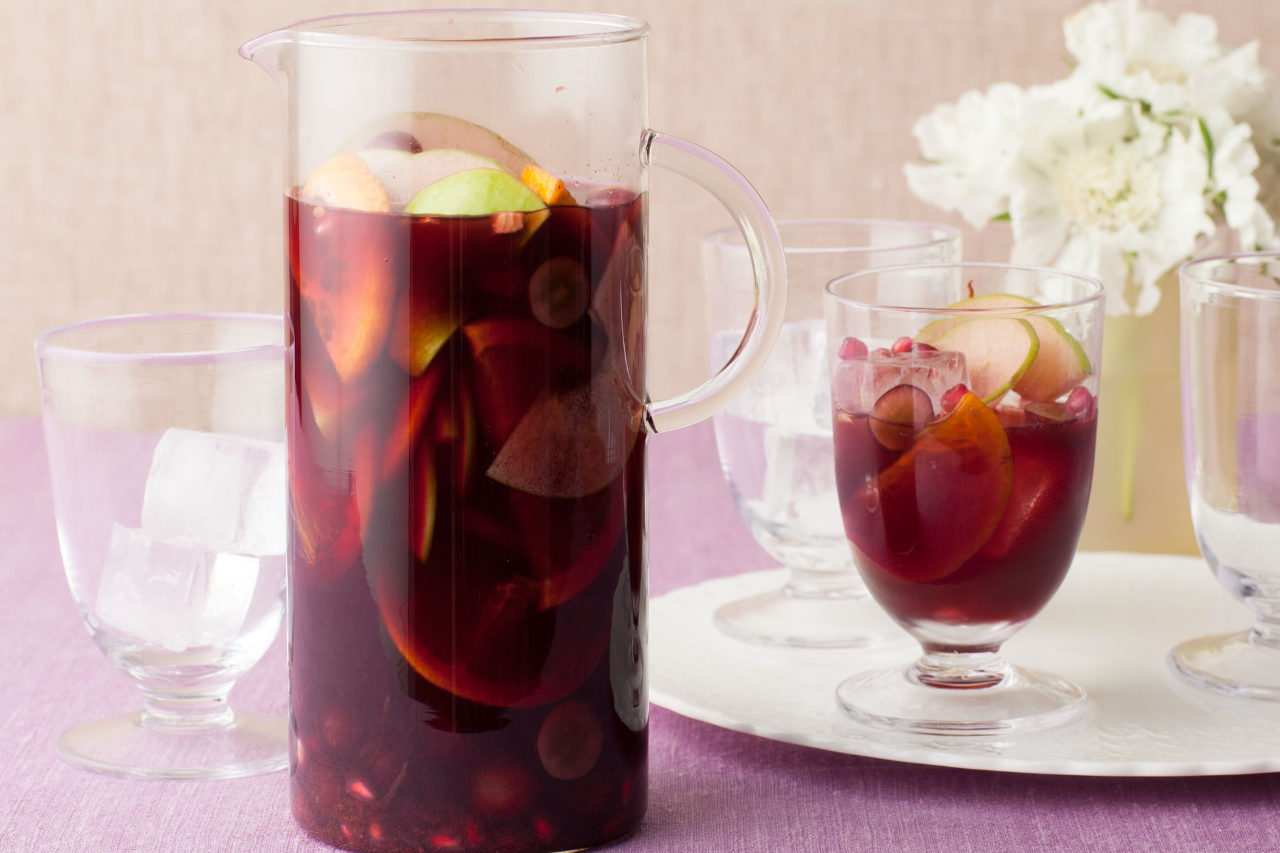 A large jug of pomegranate sangria and a few glasses with ice in them, one full of the sangria