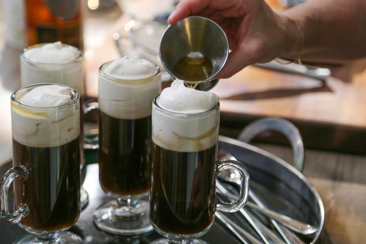 Three glass mugs of Irish coffee topped with whipped cream on a silver serving tray