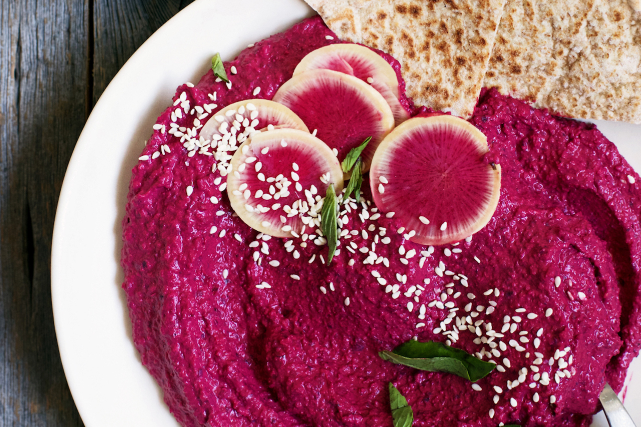 Close-up shot of red beet hummus with radishes and pita bread