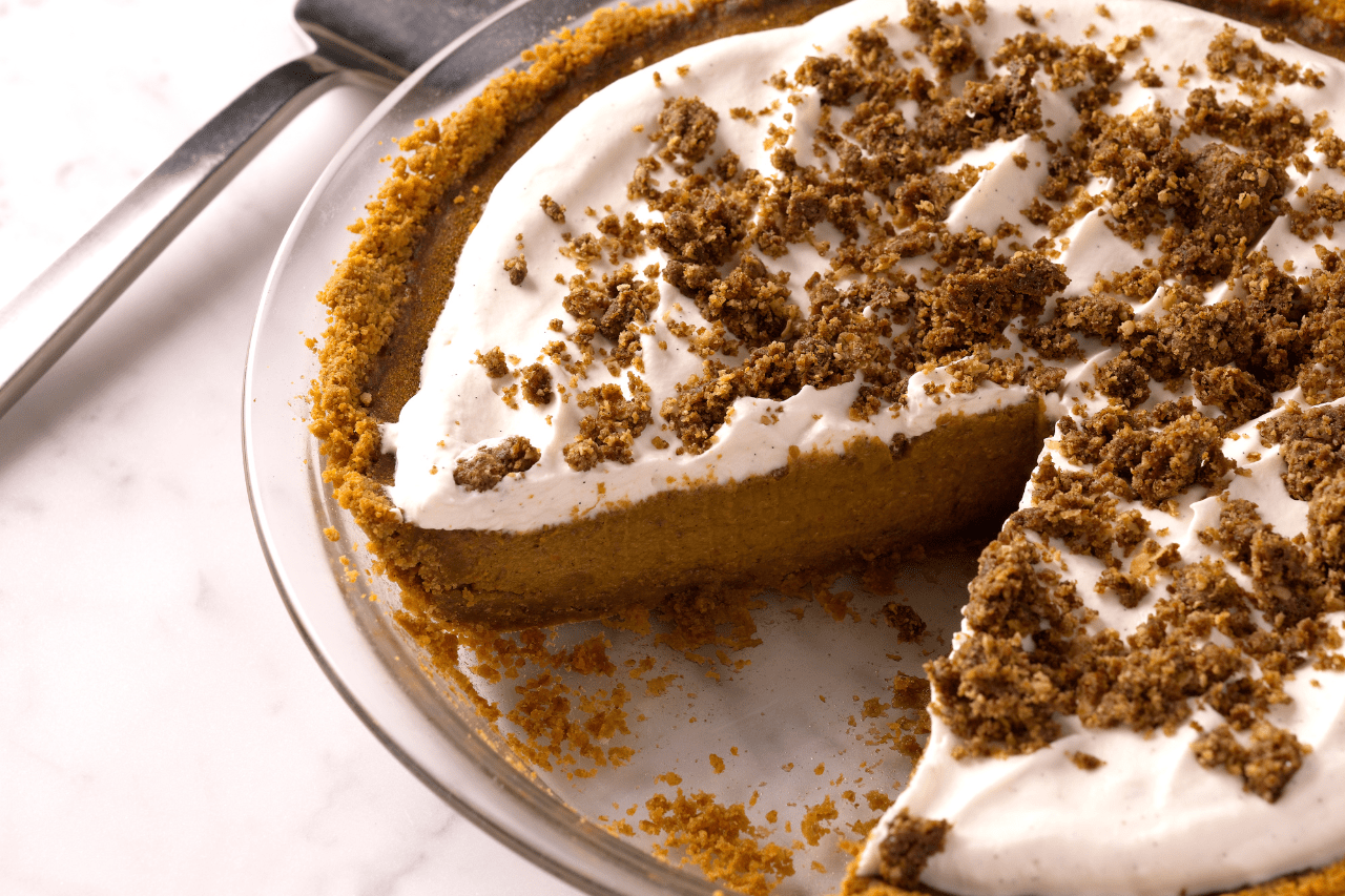 A pie tray with pumpkin pie topped with whipped cream and a cinnamon crunch topping