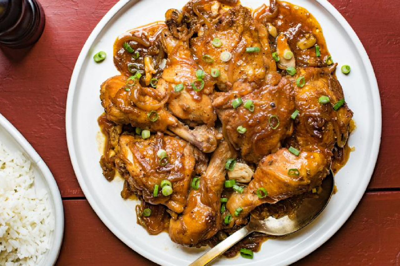 An overhead shot of a plate of Filipino chicken adobo with green scallions to garnish