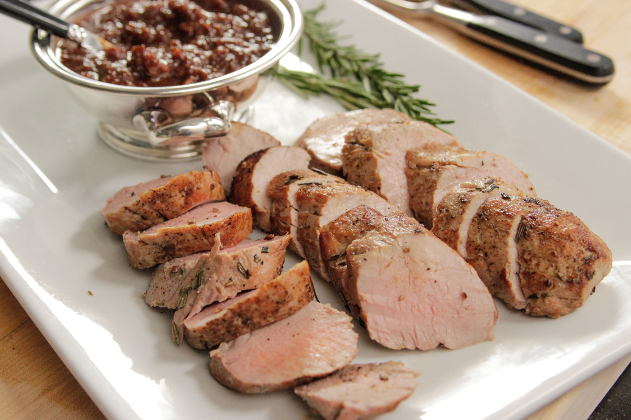 A serving platter with a sliced roasted pork tenderloin served with a sauce