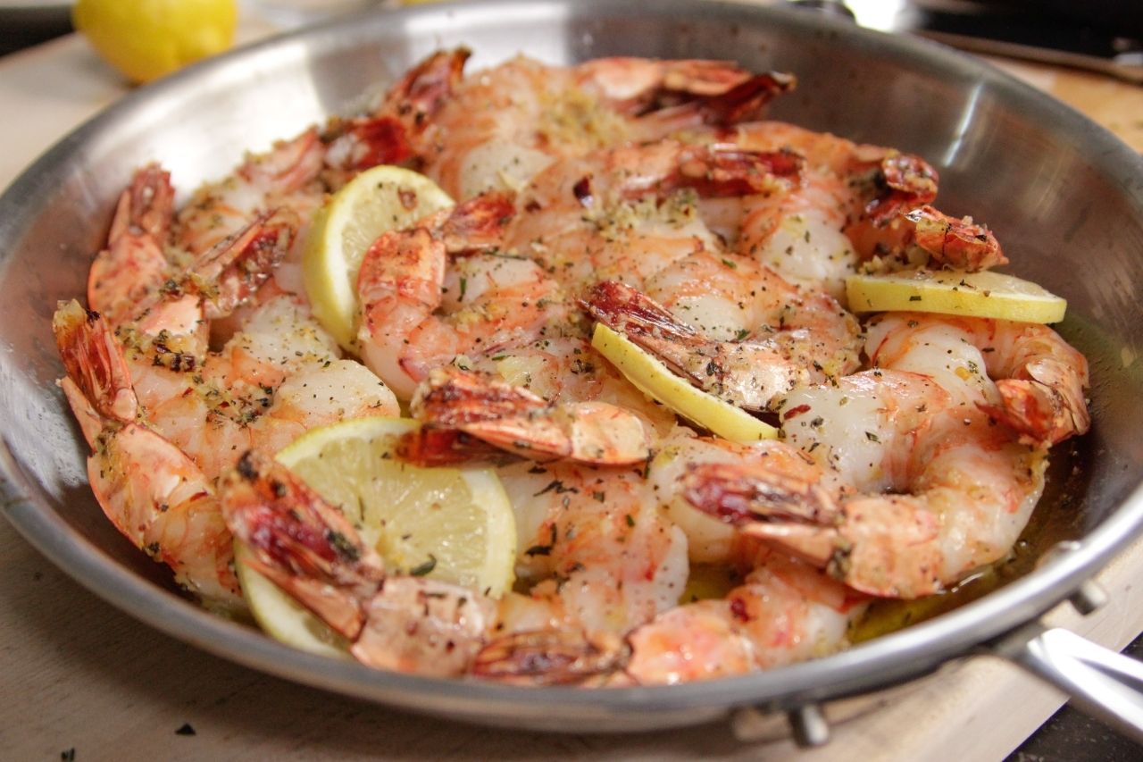 A metal pan with cooked and seasoned shrimps and a few slices of lemon