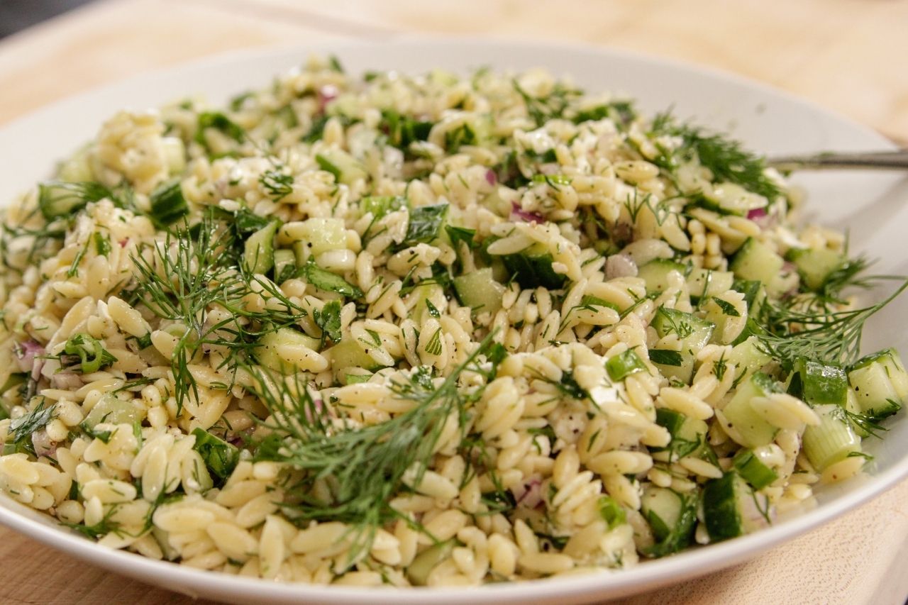 A serving bowl with orzo pasta with herbs and feta cgeese