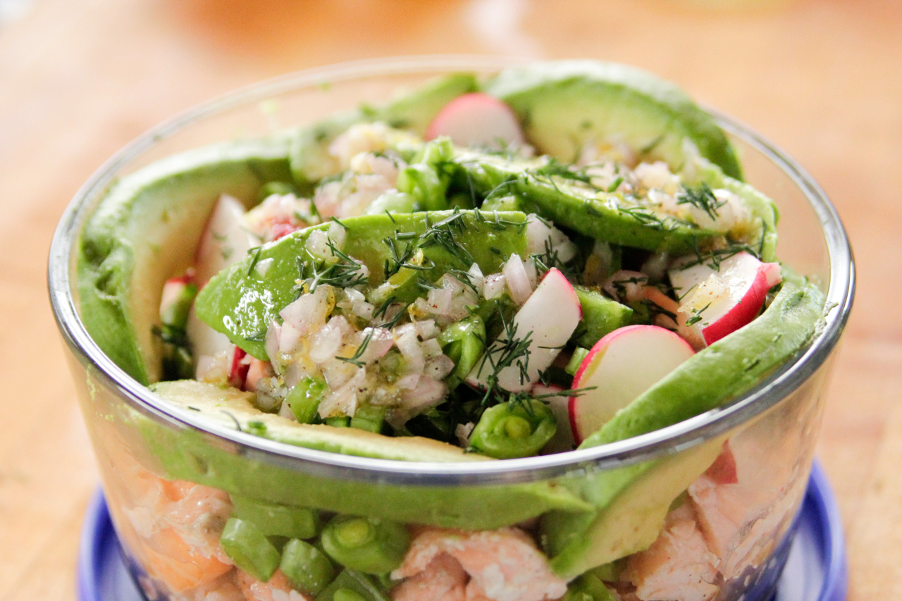 A glass bowl with avocado, fresh veggies and grains