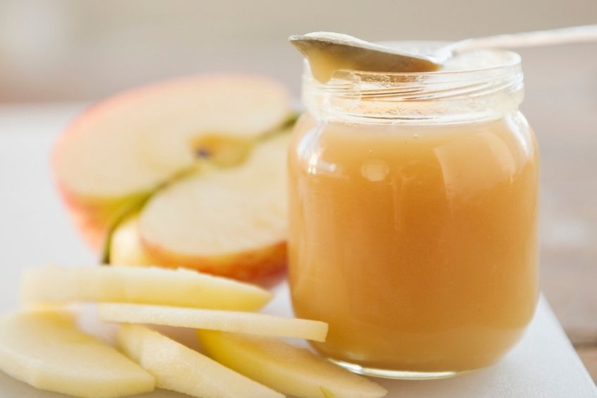 A jar of applesauce with slices of red apple