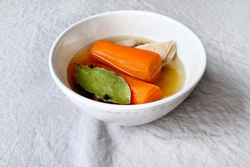 A bowl of clear broth with carrot, chicken and herbs