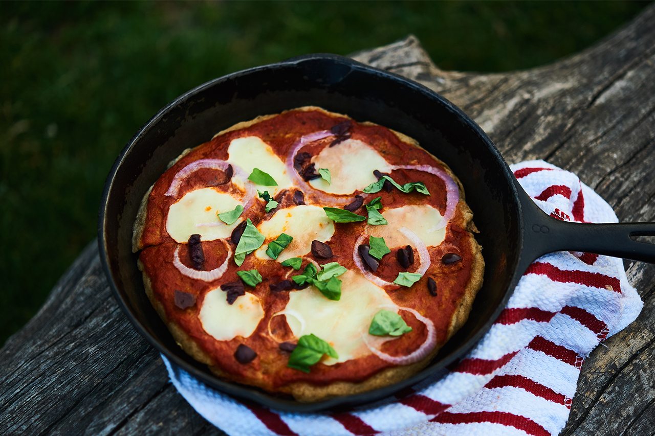 skillet near a campfire with a pizza in it