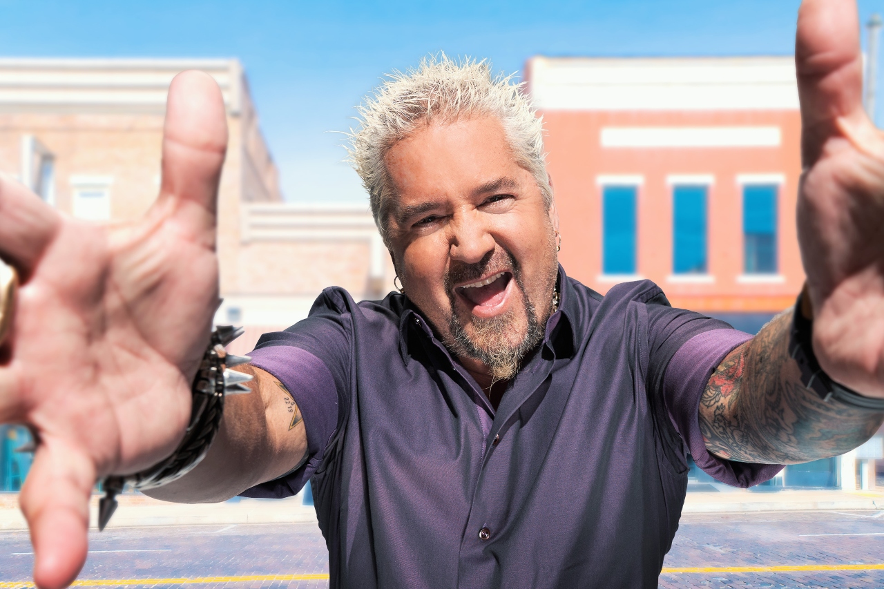 Celebrity chef Guy Fieri of Diners, Drive-Ins and Dives with his arms outstretched.