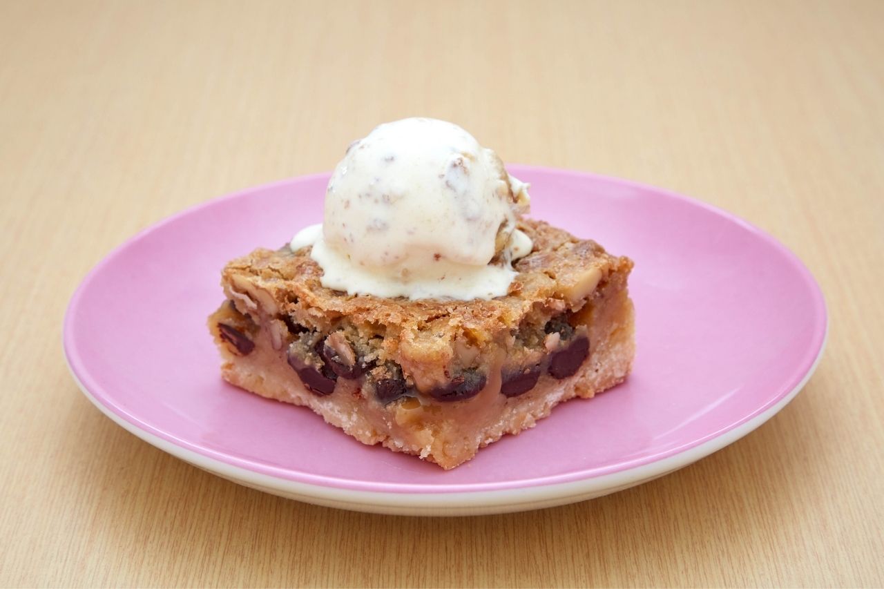 A pink plate with a square of butter tart with raisins and a scoop of ice cream