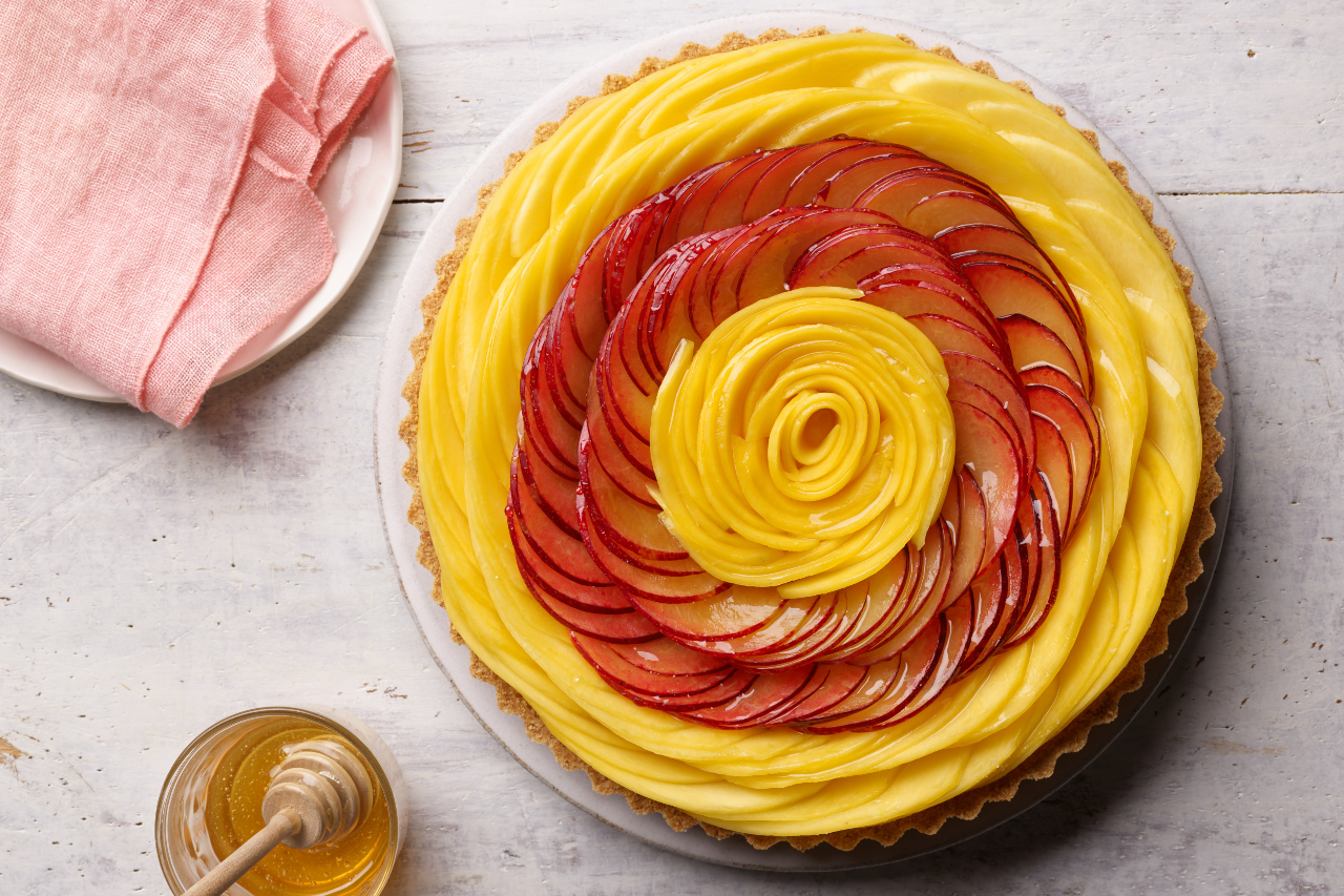A cheesecake tart with a sliced mango and plum topping that looks like a rose