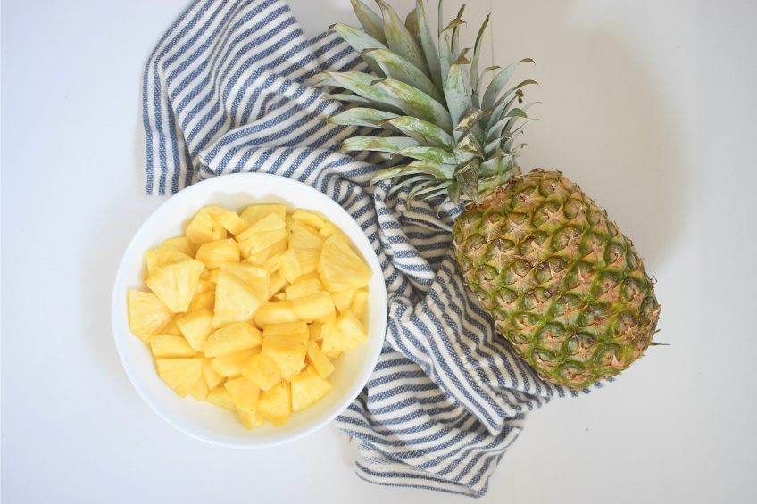 A full pineapple and a bowl of pineapple chunks