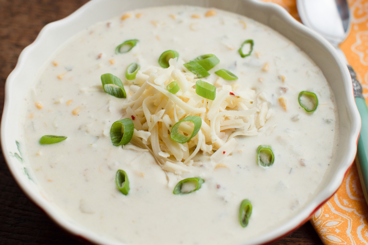 A bowl of chowder with fresh green onions and shredded cheese