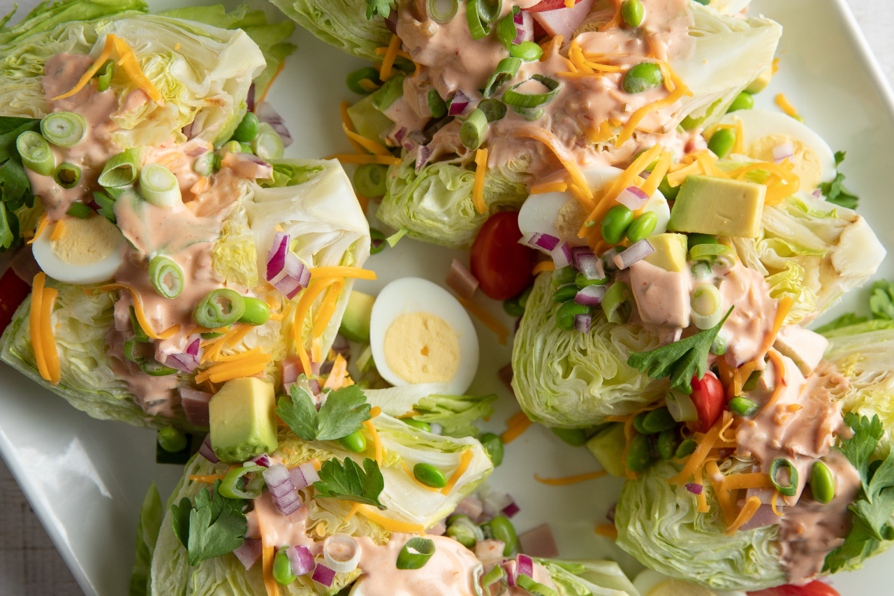 A deconstructed coobb salad with eggs, avocado chunks and wedges of iceberg lettuce