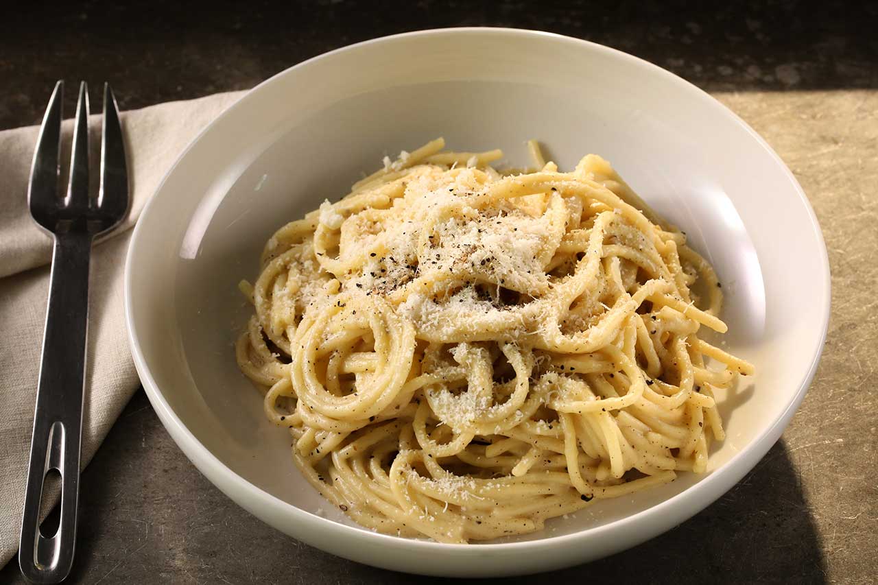 Bowl of cacio e pepe pasta on a table with a fork beside it