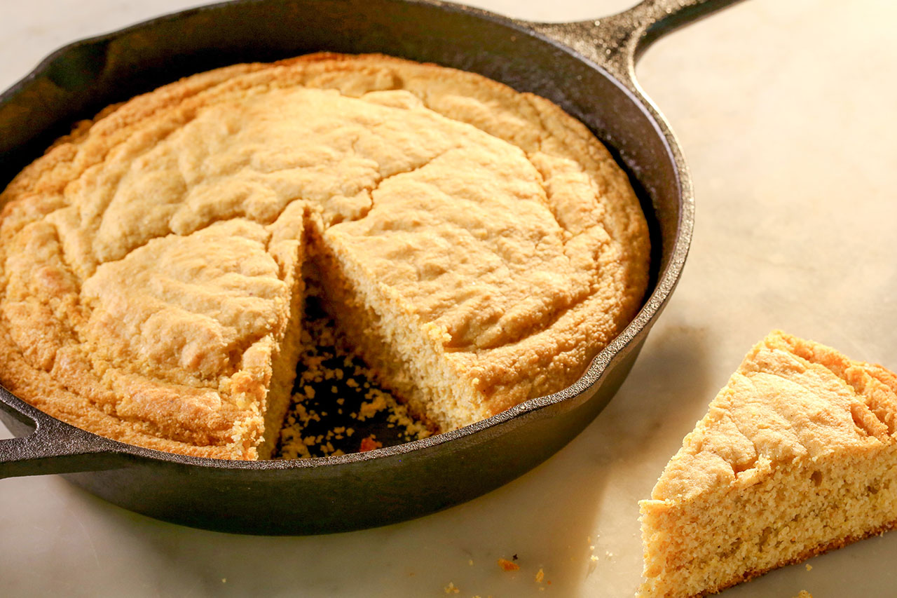 cornbread in a round skillet with a triangle piece cut out from it
