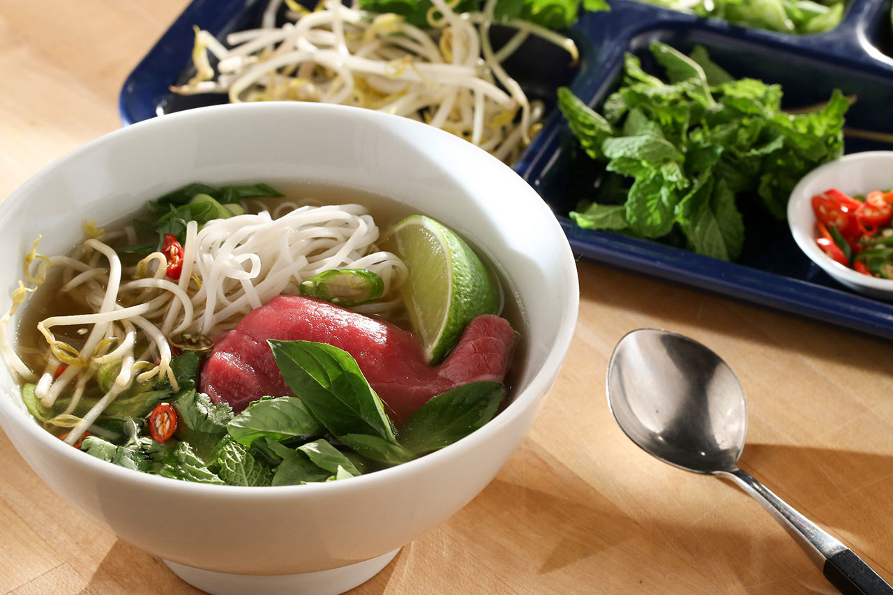 bowl of beef pho with noodles, greens and a lime wedge in the bowl of soup