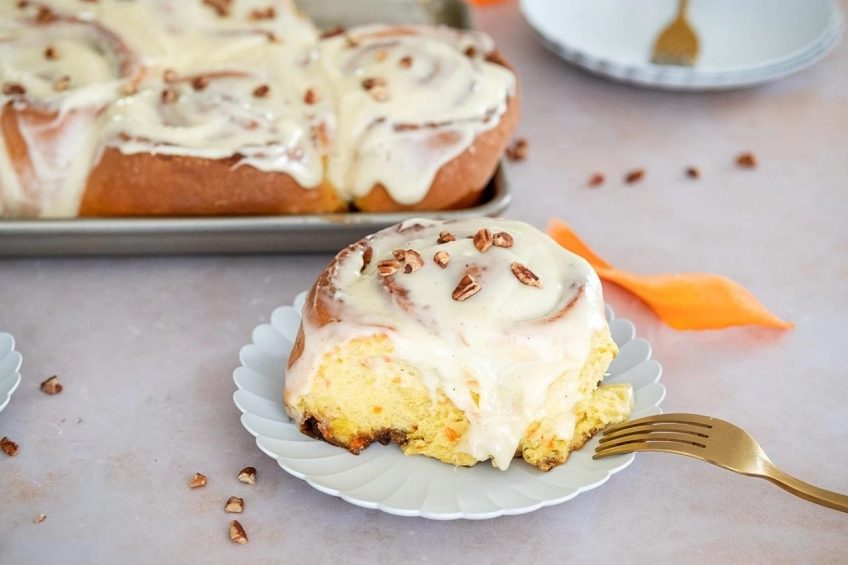 A carrot cake cinnamon roll with a healthy heap of frosting and chopped walnuts