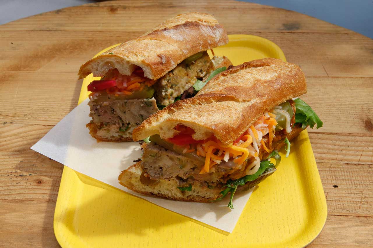 Subway-style sandwich filled with veggies and meat on a yellow plate