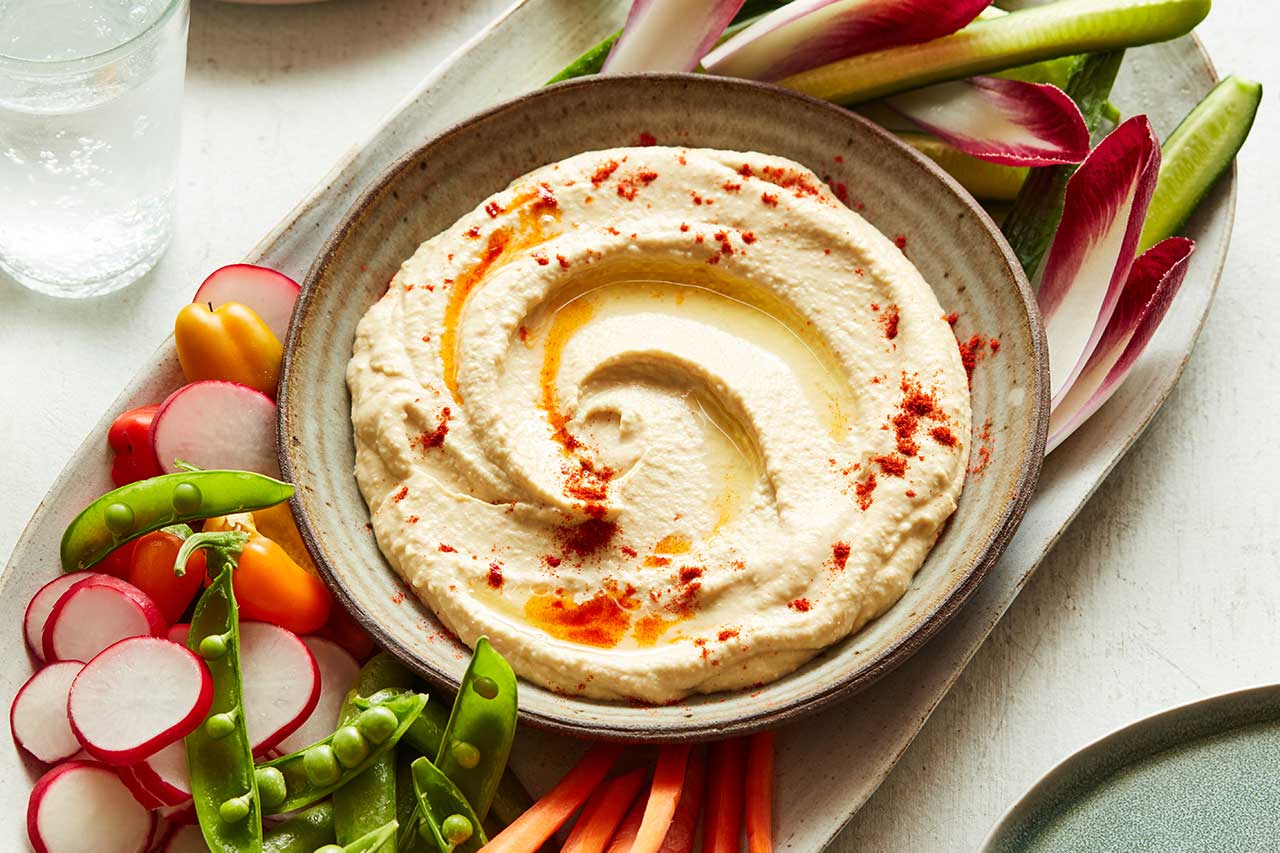 a bowl of hummus with veggies on the side on a plate