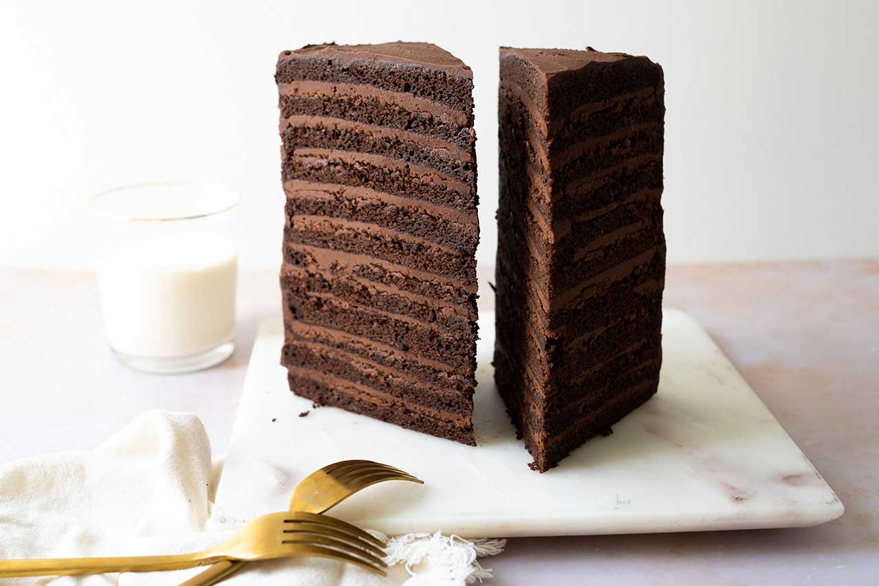 huge slice of 12-layer chocolate cake on a plate with a glass of milk