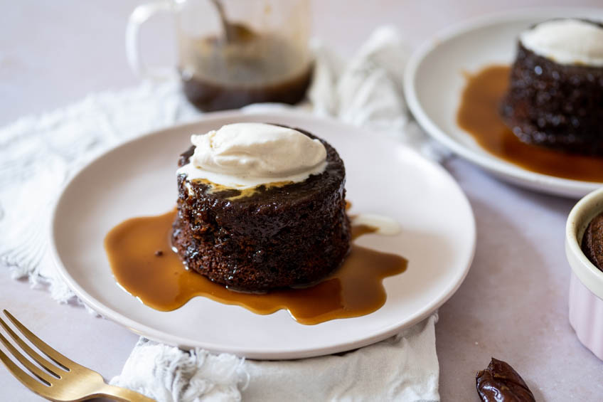 A plate with a sticky toffee pudding with caramel sauce and a dollop of ice cream