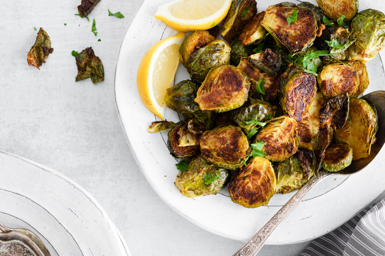 Golden brown curried Brussels sprouts on a white plate with a wedge of lemon