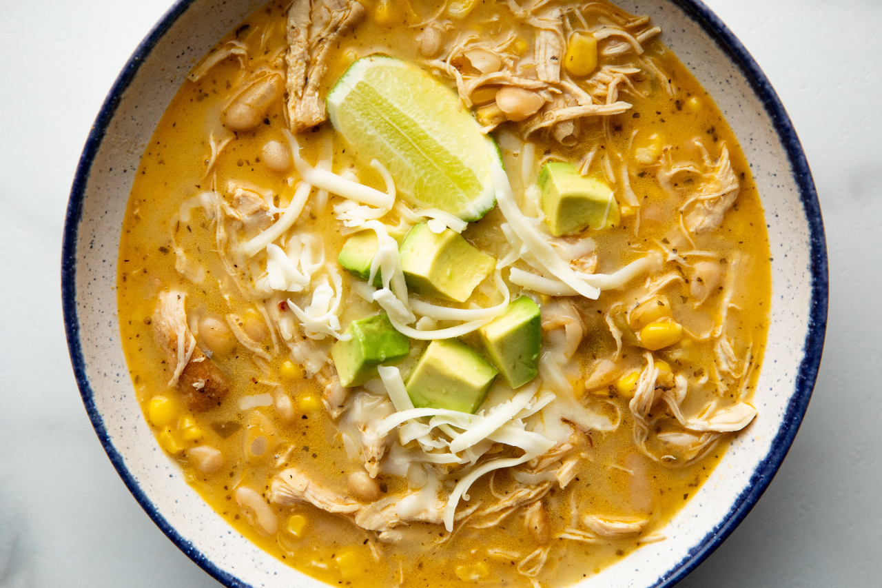 White Chicken Chili in a bowl, garnished with shredded cheese, diced avocado and a lime wedge