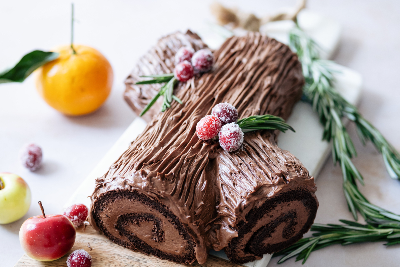 A chocolate yule log with fresh herbs, sugared raspberries and oranges nearby