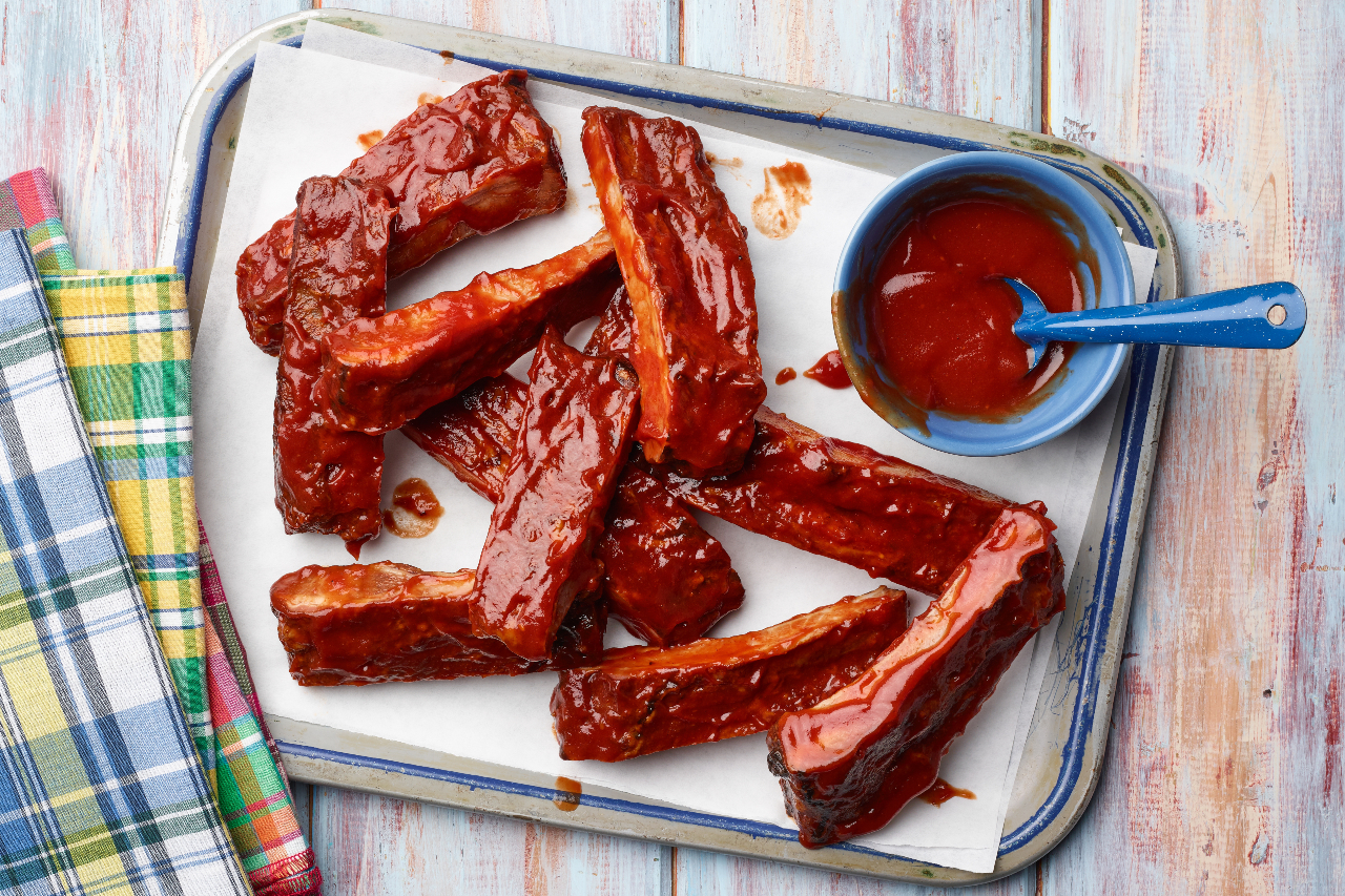 Air fryer pork spare ribs on a tray with barbecue sauce on the side