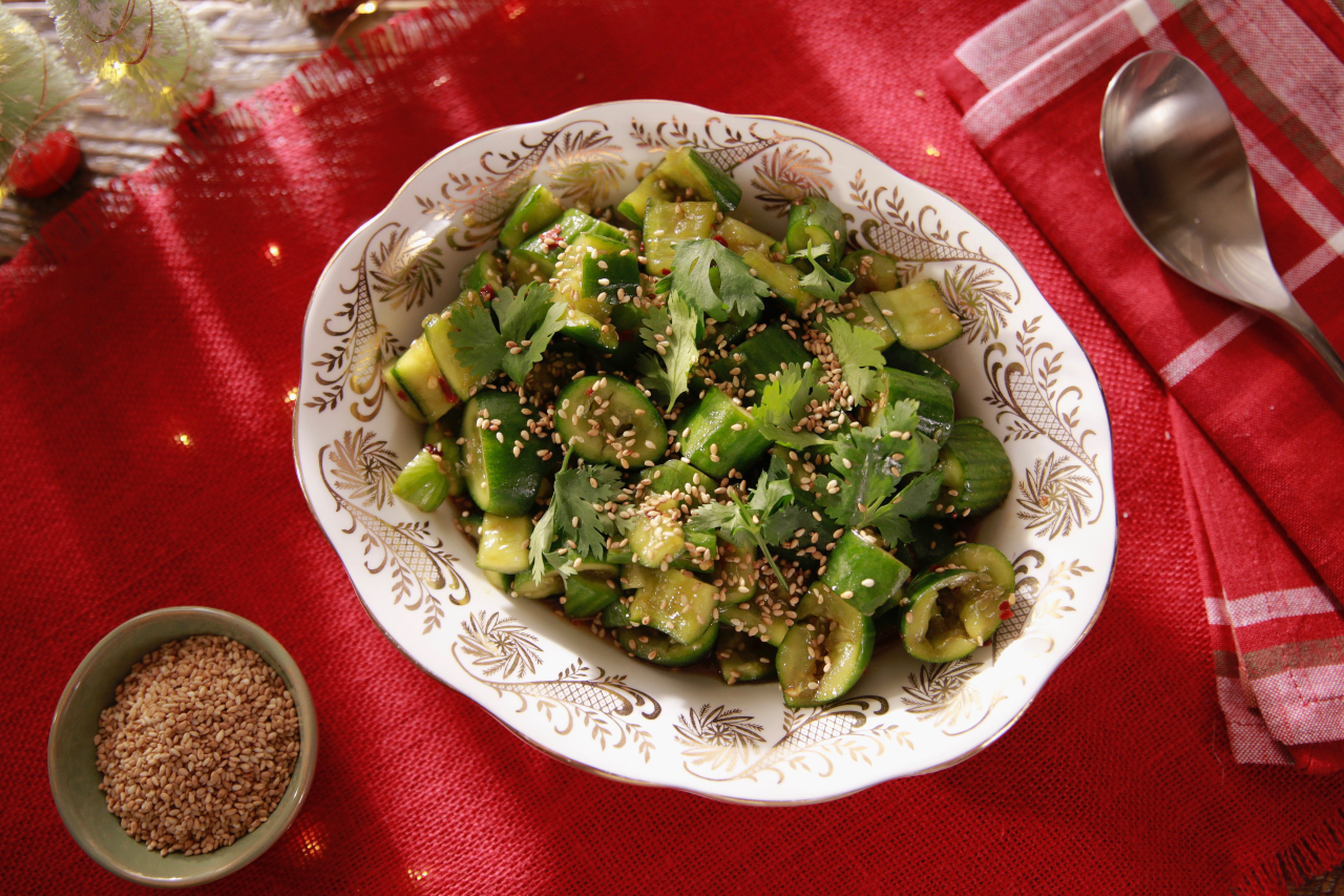 Chinese smashed cucumber salad on a white serving platter with a bowl of sesame seeds on the side