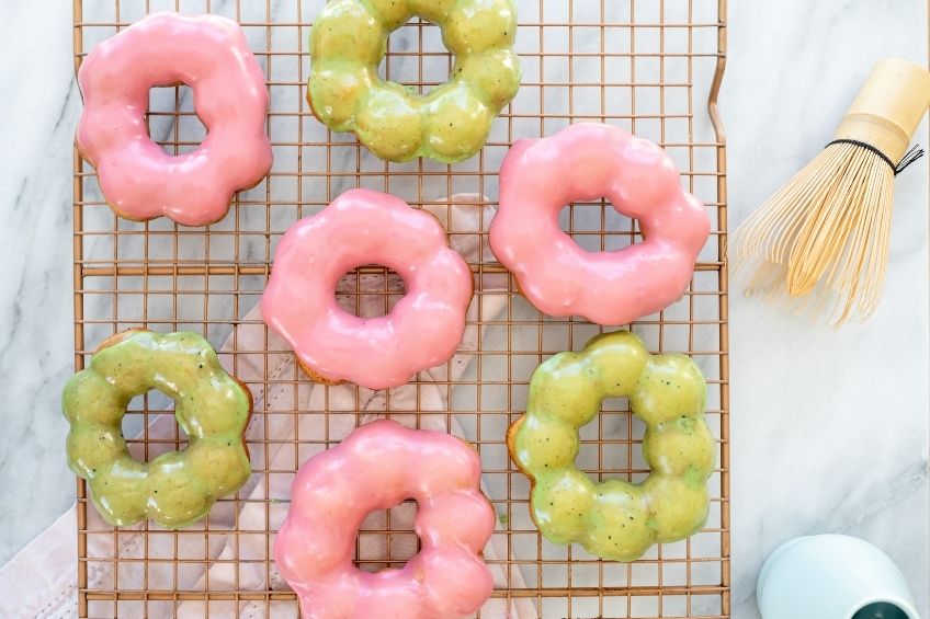 Four flower-shaped raspberry glazed doughnuts and three flower-shaped matcha green donughts on a baking tray