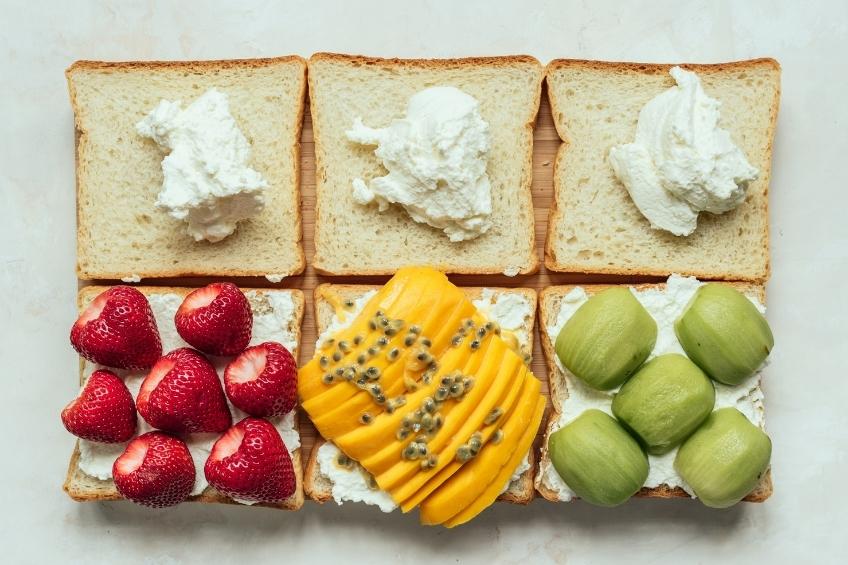 Six pieces of bread. Three are topped with whipped cream and the other three have slices of mangos, kiwis, and strawberries,