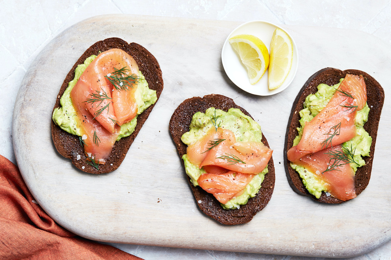 Three slices of pumpernickel bread topped with avocado and smoked salmon