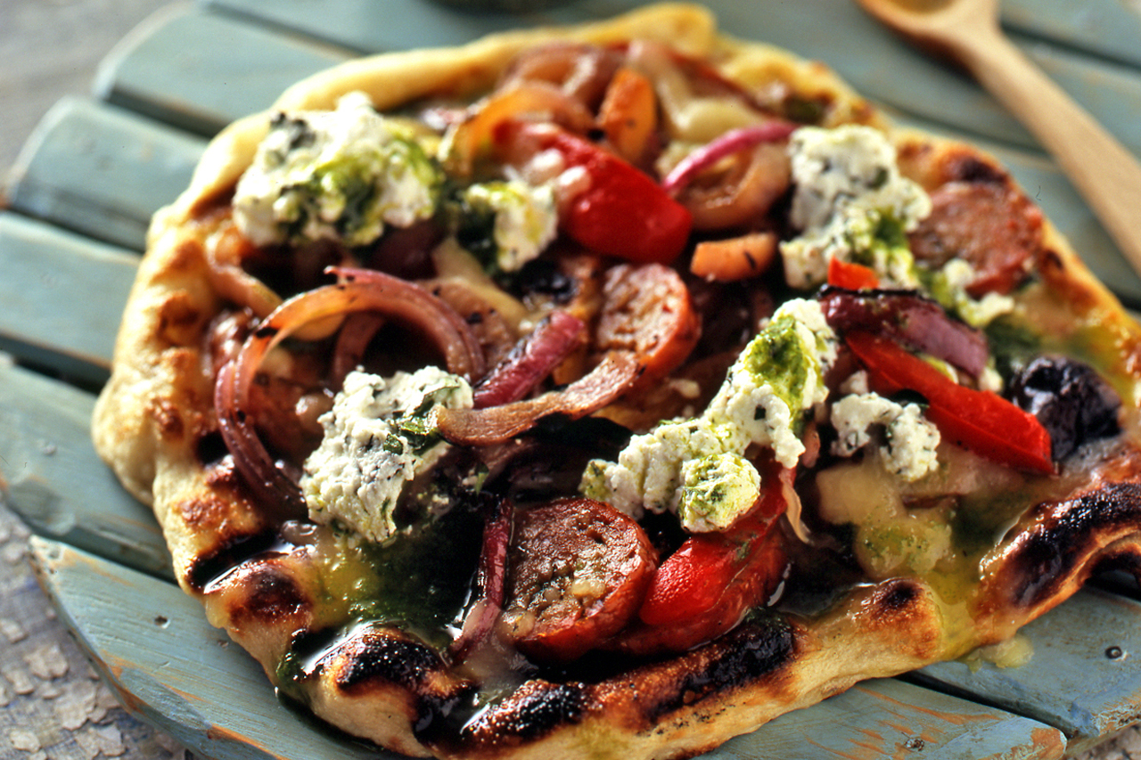 grilled pizza with hot sausage, grilled peppers and onions and oregano ricotta on a serving tray