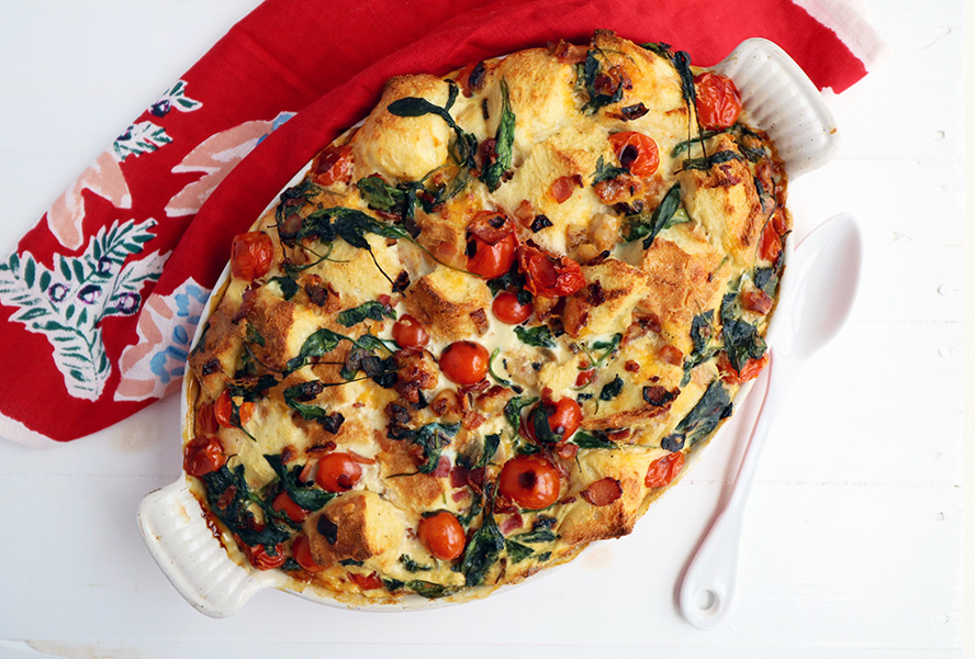 An oval dish with a green and red strata studded with spinach and cherry tomatoes