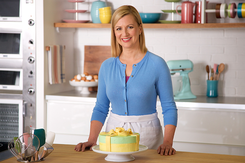Anna Olson poses smiling with her hat box birthday cake