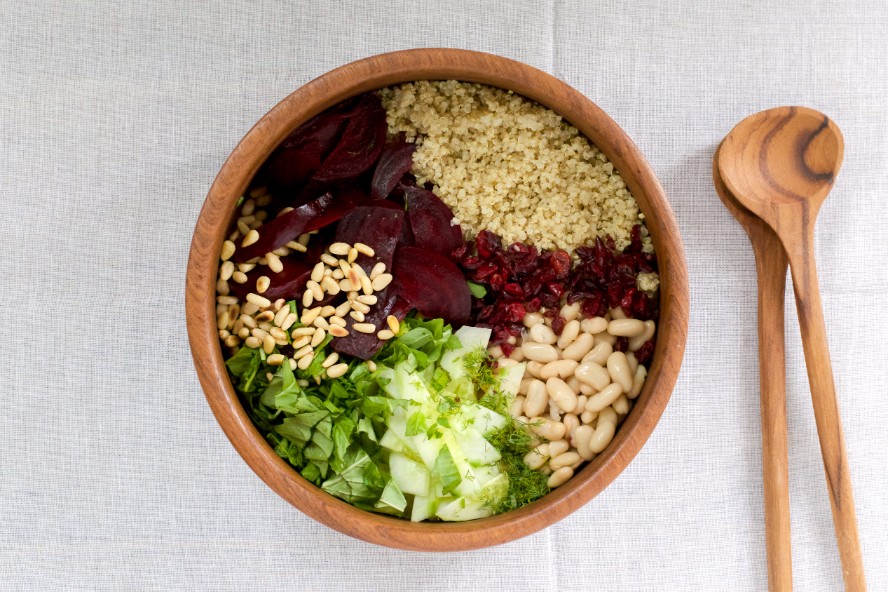 A wooden bowl with the ingredients for a summer salad in sections: quinoa, beets, toasted nuts, iceberg lettuce and white beans